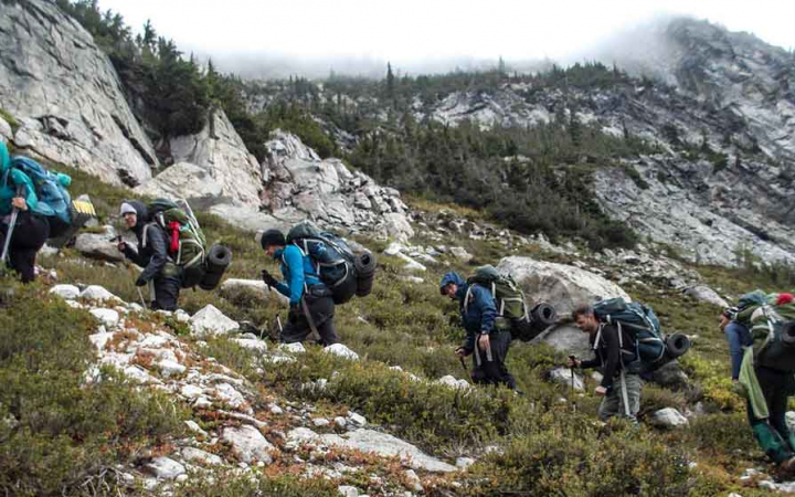 teens backpacking through rocks and greenery on outward bound course